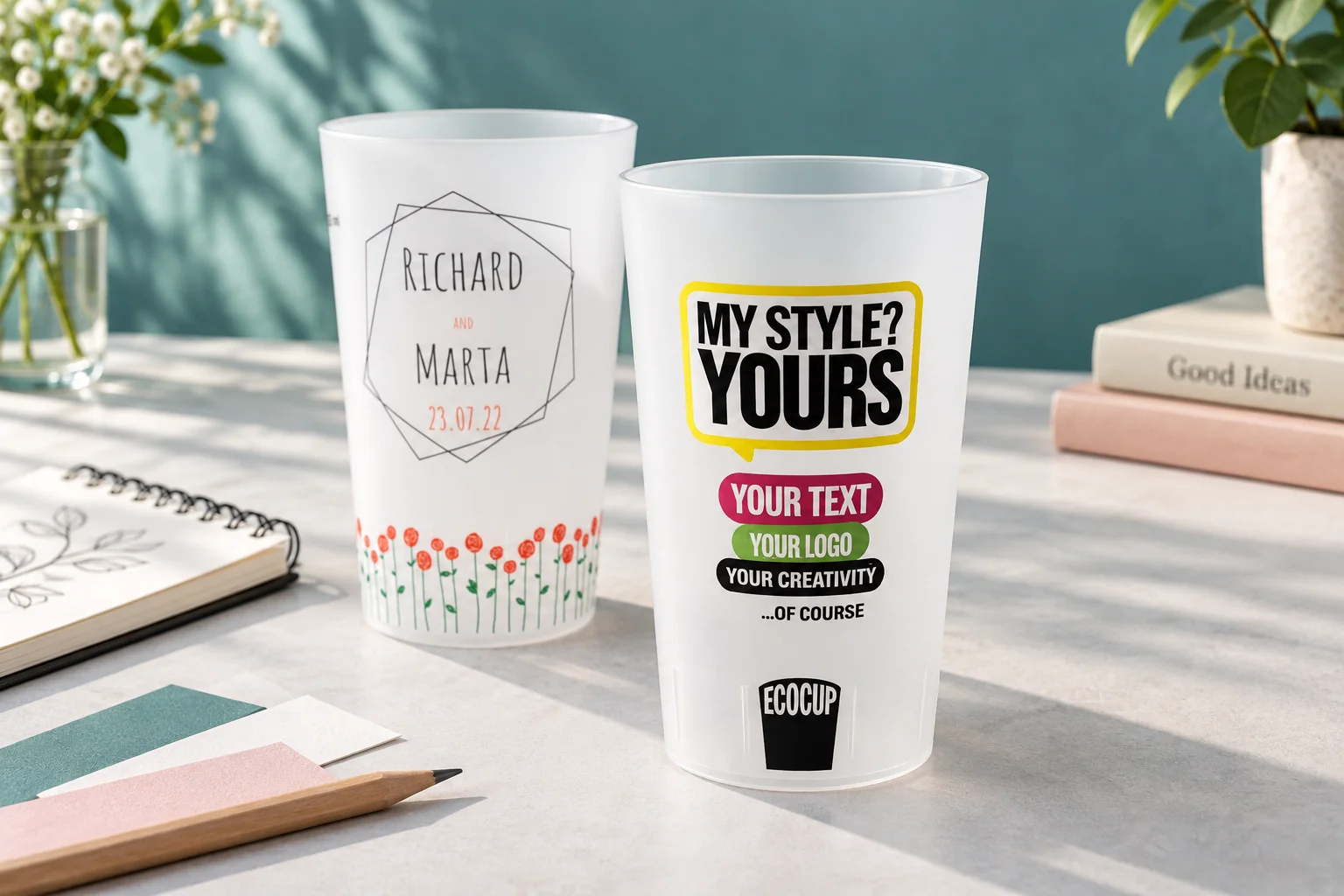 Two personalised ECO 30 Half pint cups with colourful lettering and a floral wedding design on a creative studio table